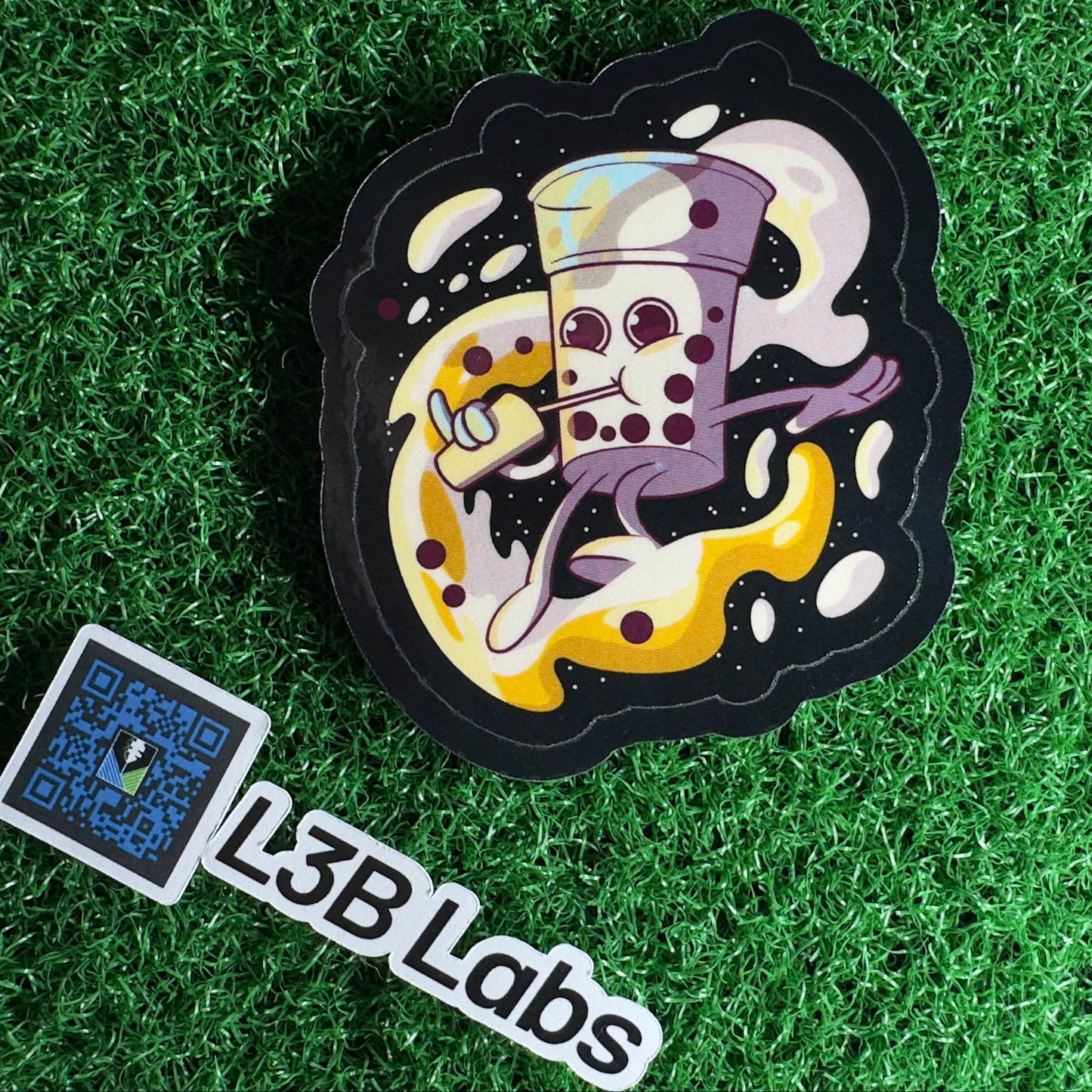 Sticker with a cartoon character the shape of a boba tea drinking coffee on a grass background