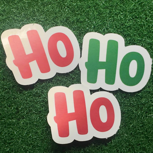 A sticker on a grass background with the sticker saying Ho Ho Ho with 2 in red and 1 in green